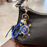 Blue turtle evil eye keychain clipped to a black handbag, with a blue braided loop and blue shell accents.