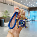Blue turtle evil eye keychain held upright, showing blue shell accents, a blue braided loop and gold tone hardware.