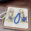White and blue turtle evil eye keychains arranged on a tray, showing their loops, round rings and clasps.