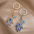 Gold tone and silver tone openwork Hamsa keychains side by side, with blue eyes along the fingers and separate round eye charms.