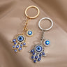 Gold tone and silver tone openwork Hamsa keychains side by side, with blue eyes along the fingers and separate round eye charms.