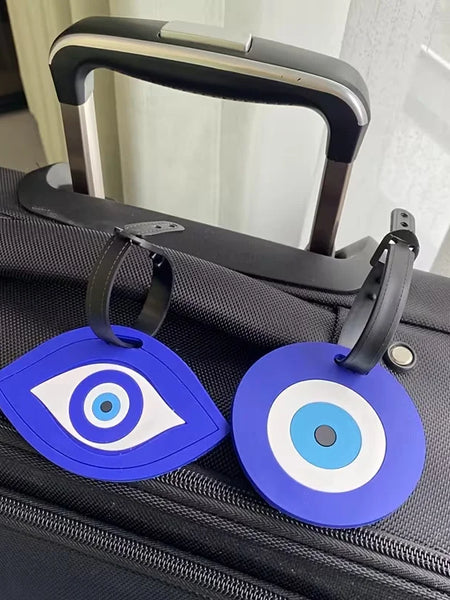 Blue almond-eye and round luggage tags with black buckle straps resting across the top of a black suitcase.