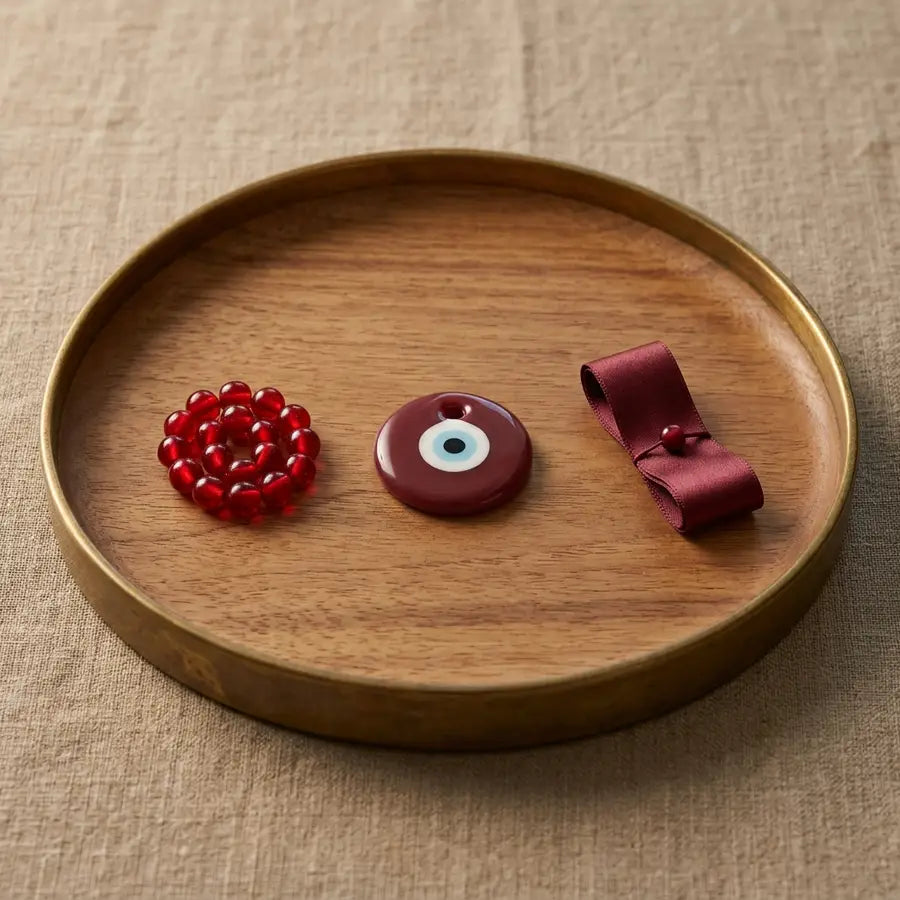 Red beads, a central maroon evil eye charm, and a burgundy ribbon arranged as related protective tones.