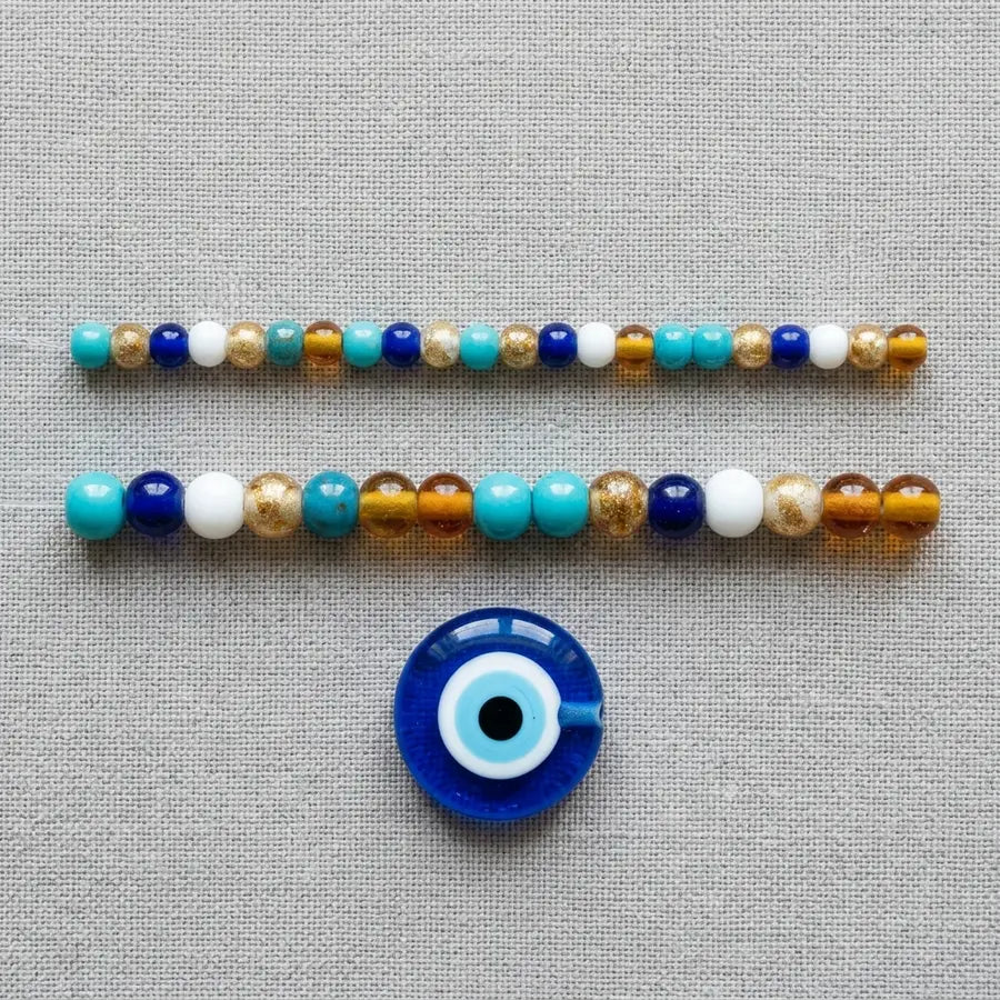 Two parallel bead rows of visibly different sizes with a larger evil eye focal bead centered below for scale.