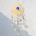 Gold tone eye and crescent suncatcher with a blue eye center, blue beads and five round faceted drops.