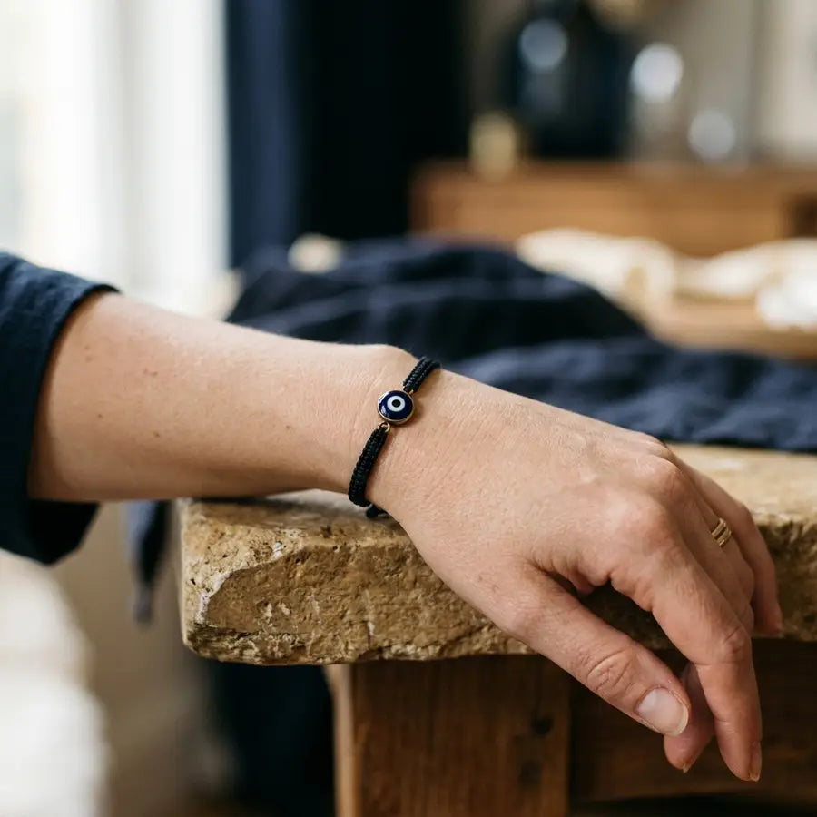 Black evil eye bracelet sharp on a relaxed wrist with a soft circular shadow boundary blurred behind it.