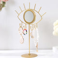 Gold tone eye tabletop mirror with bracelets and pendants hanging from the hooks beneath it