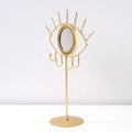 Angled view of a gold tone eye tabletop mirror showing the circular rim and four curved hooks