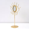 Angled view of a gold tone eye tabletop mirror showing the circular rim and four curved hooks