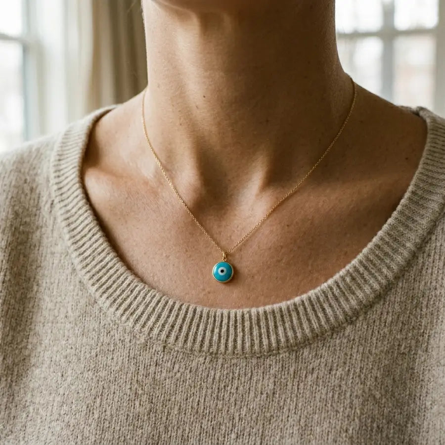 Turquoise evil eye necklace worn near the collarbone over a neutral knit top in soft daylight.