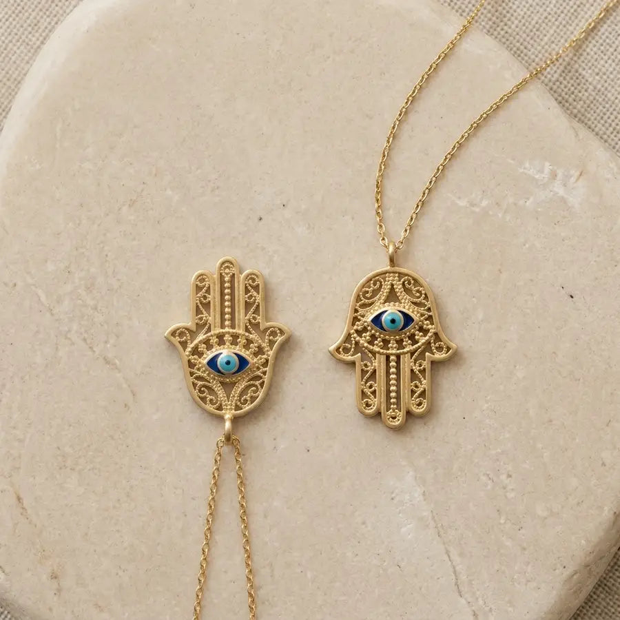 Two identical gold Hamsa charms side by side, one with fingers pointing up and one with fingers pointing down.