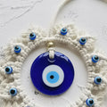 Close-up of the glossy blue evil eye disc, gold tone accent bead and small eye beads along the off-white cord frame.