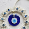 Close-up of the glossy blue evil eye disc, gold tone accent bead and small eye beads along the off-white cord frame.