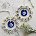 Two blue and off-white circular evil eye wall hangings arranged diagonally on a pale textured surface beside white flowers.