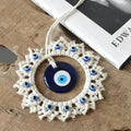 Closer oblique view of the blue evil eye disc and beaded off-white fringe on a wood surface, with the hanging cord extending upward.