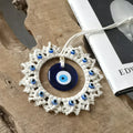 Blue evil eye wall hanging with an off-white fringed frame resting on a wood surface beside a book.