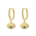Gold tone hoops with clear accents and horizontal blue evil eye charms with grooved lash details