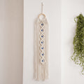 Off-white macrame wall hanging with seven blue eye accents, a circular top ring and long fringe
