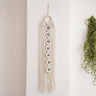 Off-white macrame wall hanging with seven blue eye accents, a circular top ring and long fringe