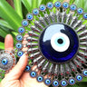 Blue evil eye pendant held in a hand, showing the silver tone sunburst frame and smaller eye motifs