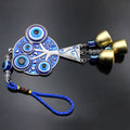 Blue evil eye tree charm with three gold tone bells and a blue loop on a dark background